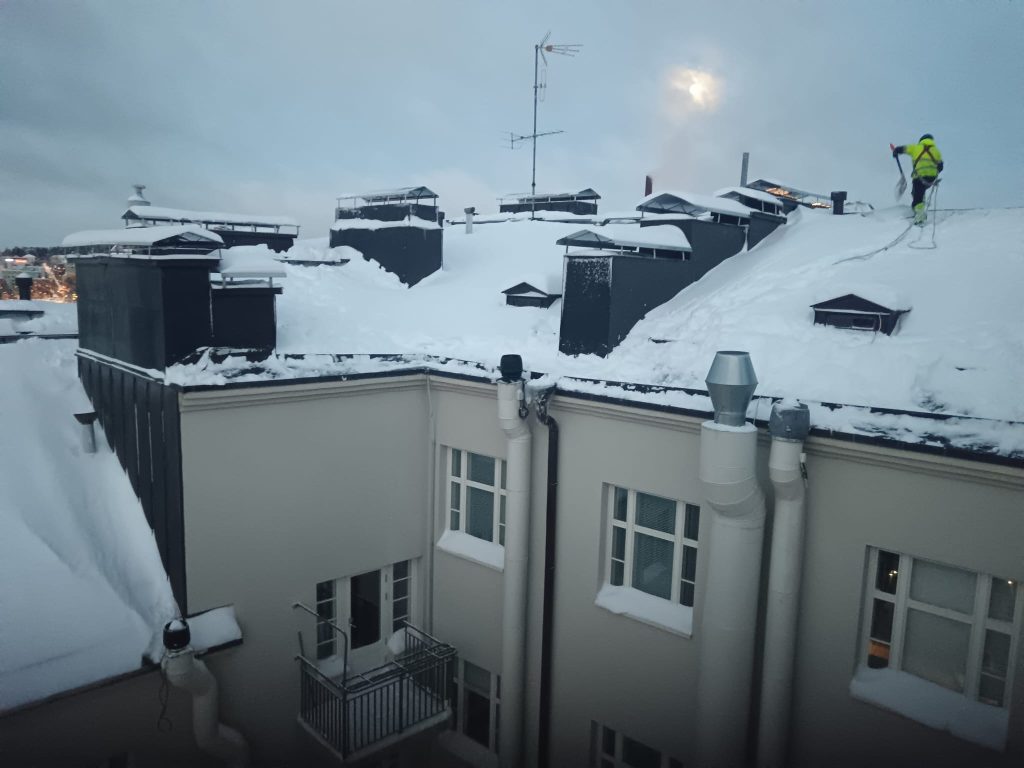 Lumenpudottaja pudottamassa lunta kerrostalon katolta